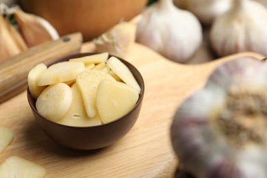 Photo of Fresh sliced garlic cloves in bowl on wooden table, closeup. Organic product