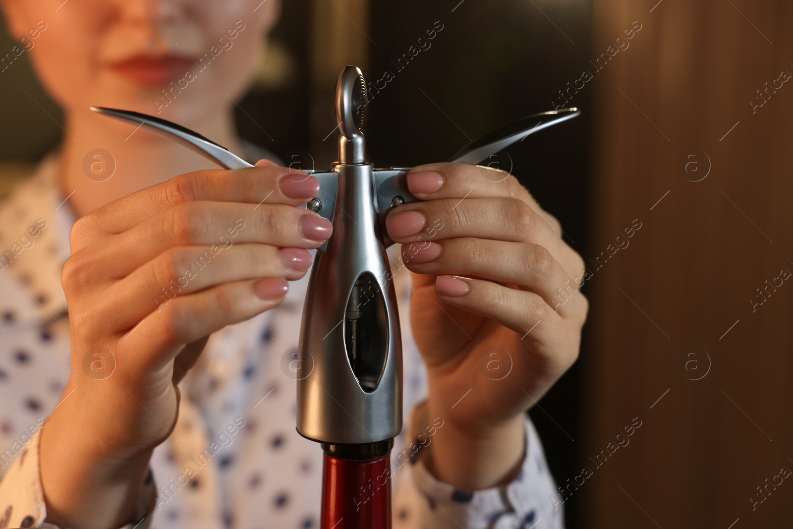 Photo of Woman opening wine bottle with corkscrew indoors, closeup