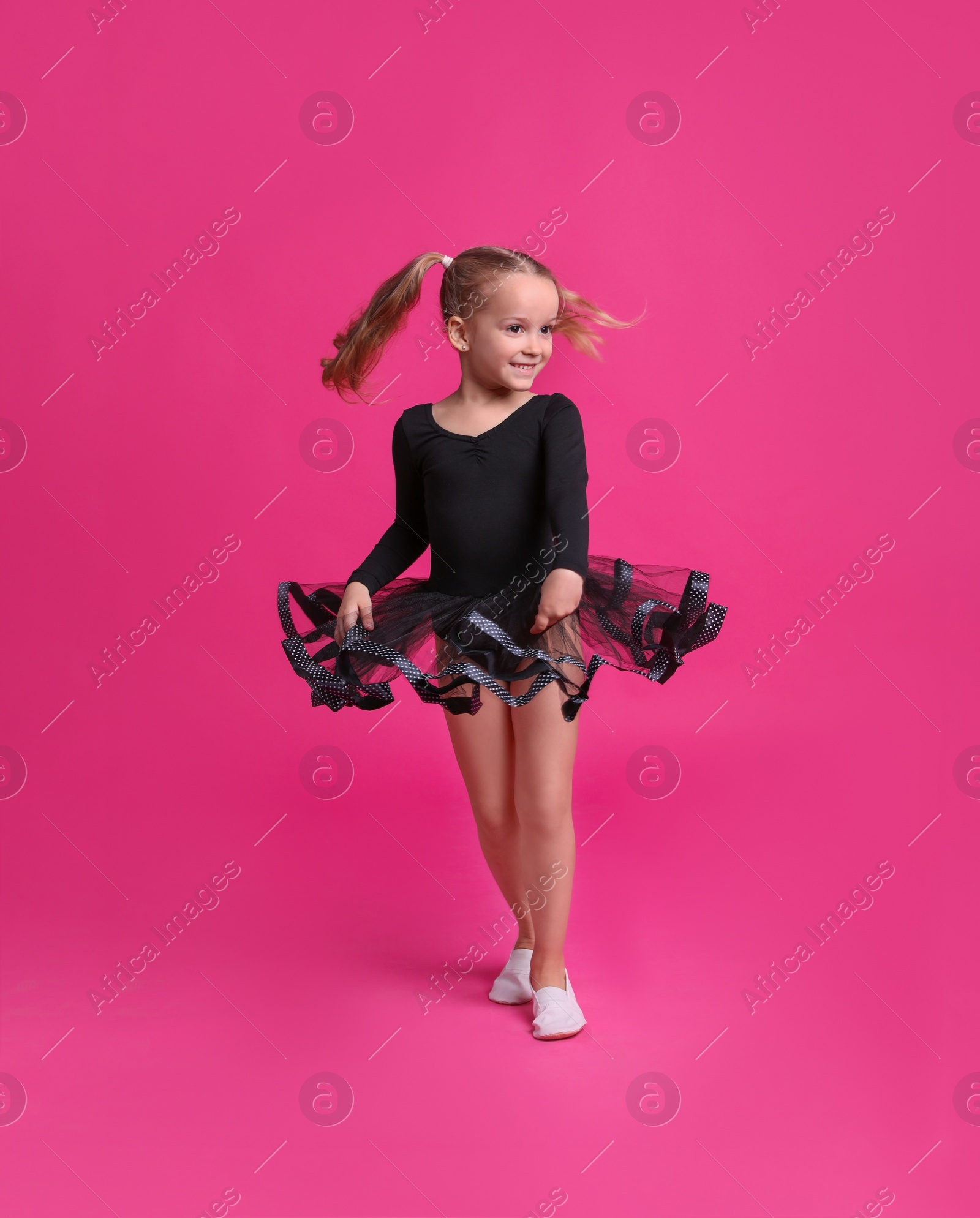 Photo of Cute little girl in black dress dancing on pink background