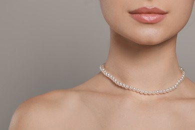 Photo of Young woman wearing elegant pearl necklace on grey background, closeup. Space for text