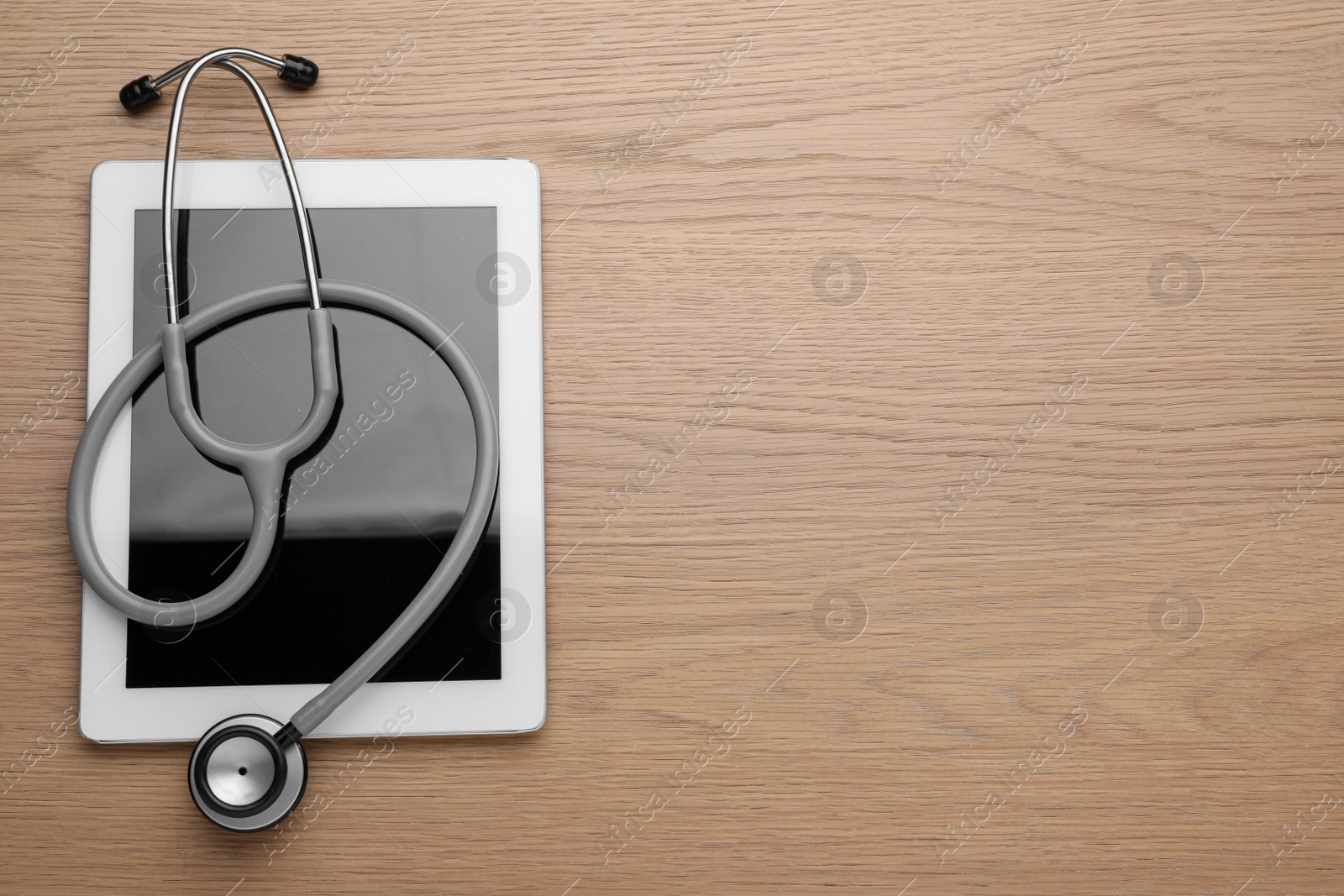 Photo of Computer tablet with stethoscope on wooden table, top view. Space for text