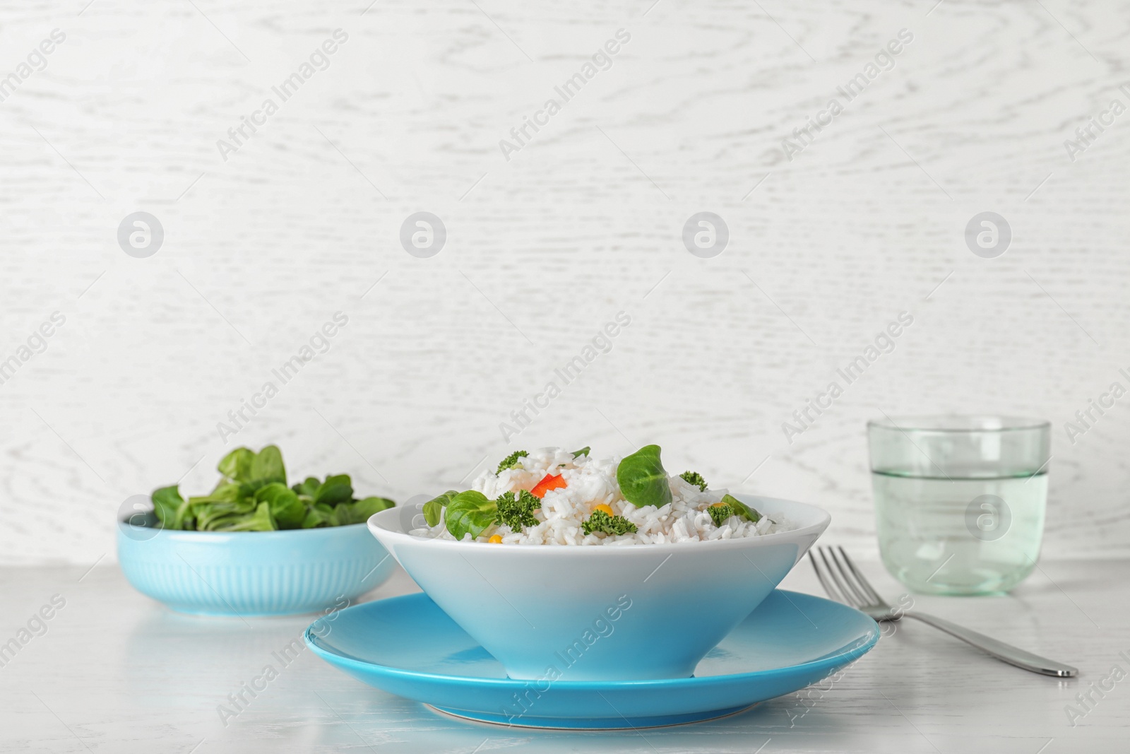 Photo of Plate of boiled rice with vegetables on table against light background. Space for text