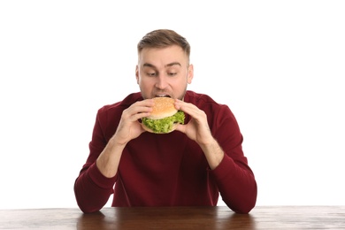 Young man eating tasty burger at table on white background