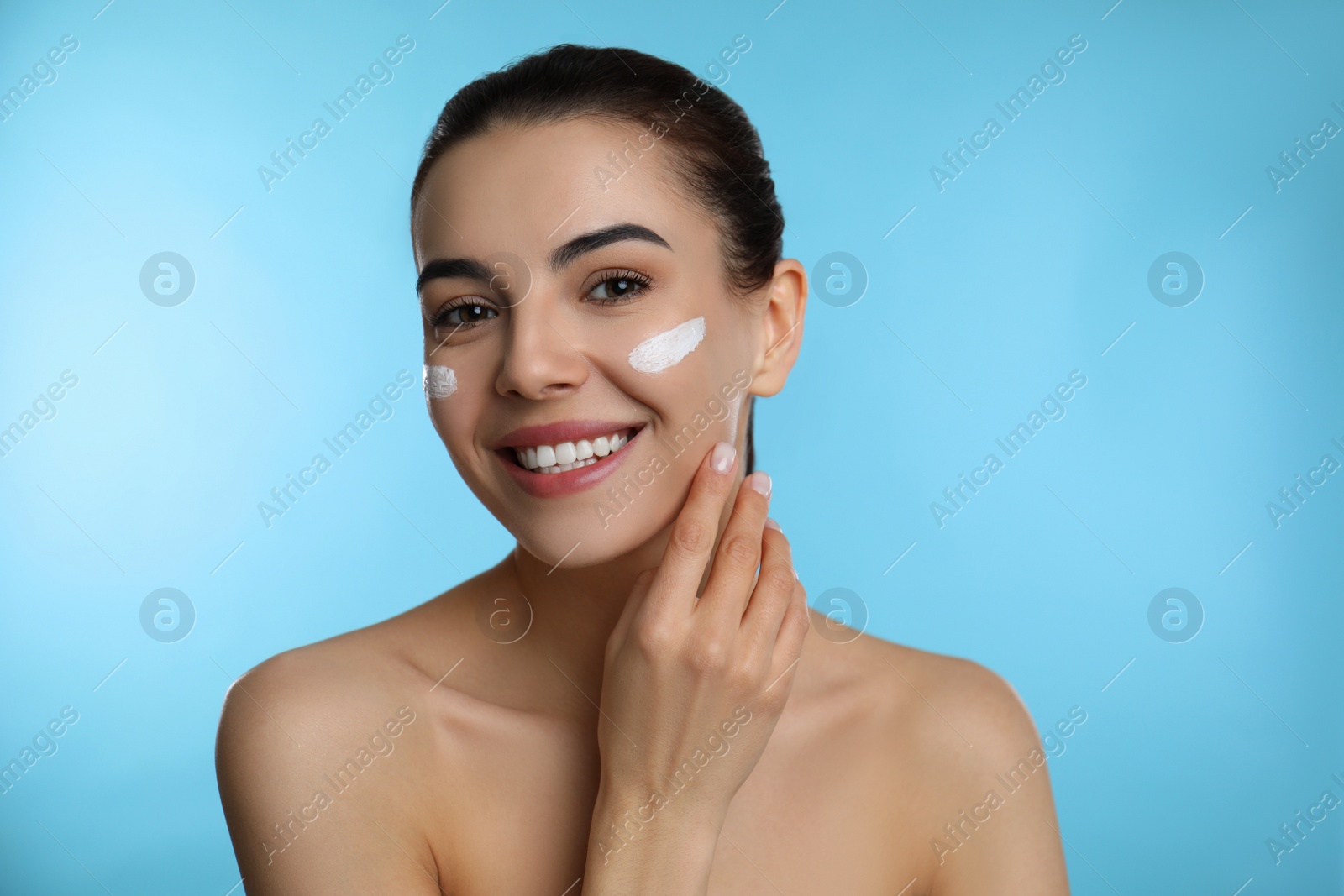 Photo of Young woman applying facial cream on light blue background