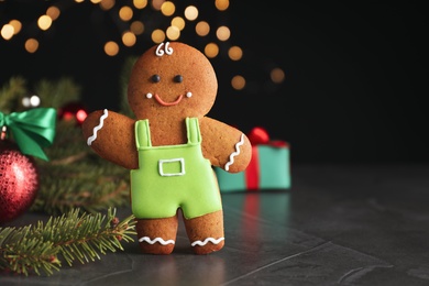 Photo of Gingerbread man on black table against blurred lights, closeup. Space for text