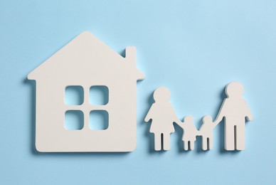 Family and house figures on light blue background, flat lay