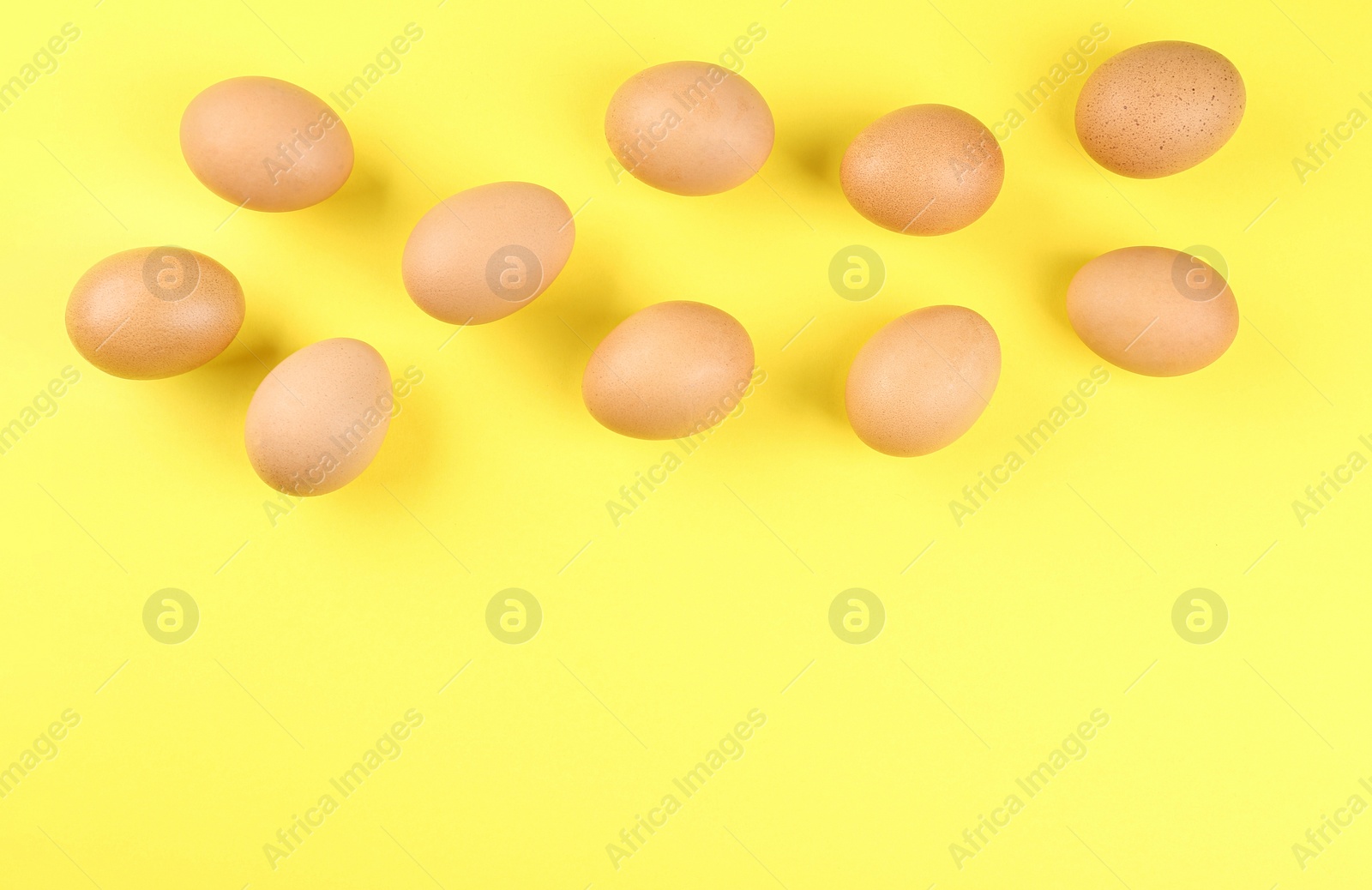 Photo of Raw chicken eggs on yellow background, flat lay. Space for text