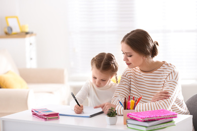 Photo of Woman helping her daughter with homework at table indoors