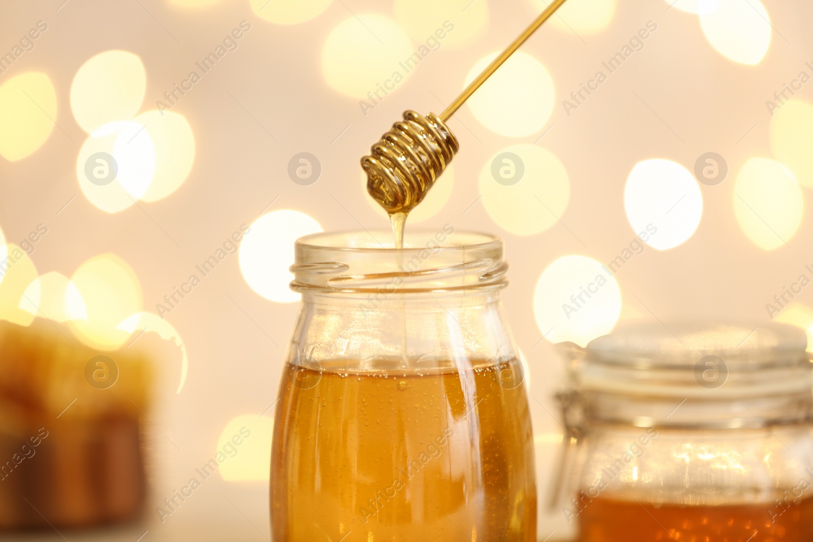Photo of Honey dripping from dipper into jar against blurred lights, closeup