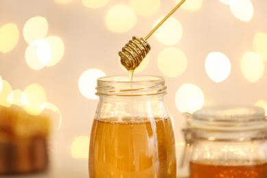 Photo of Honey dripping from dipper into jar against blurred lights, closeup