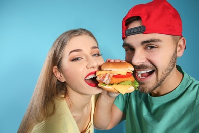 Happy couple eating burger on color background