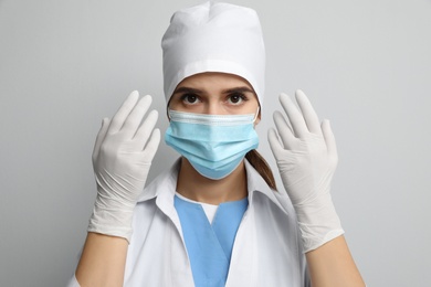 Doctor in protective mask and medical gloves against light grey background