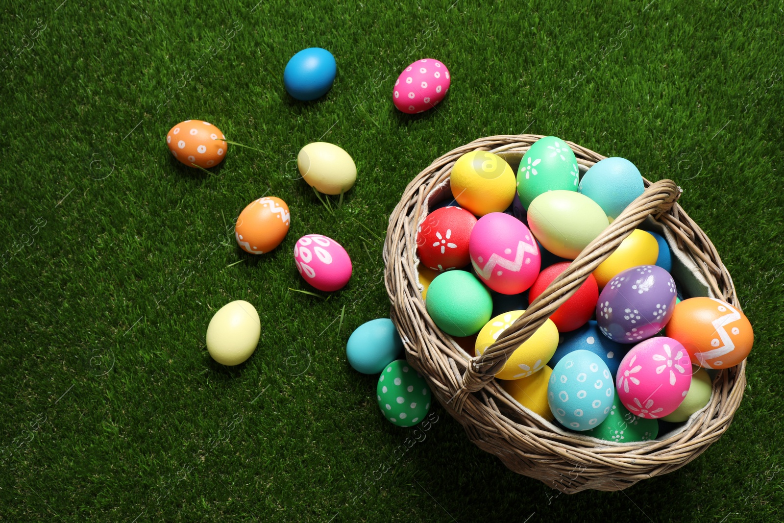 Photo of Colorful Easter eggs in basket on green grass, above view