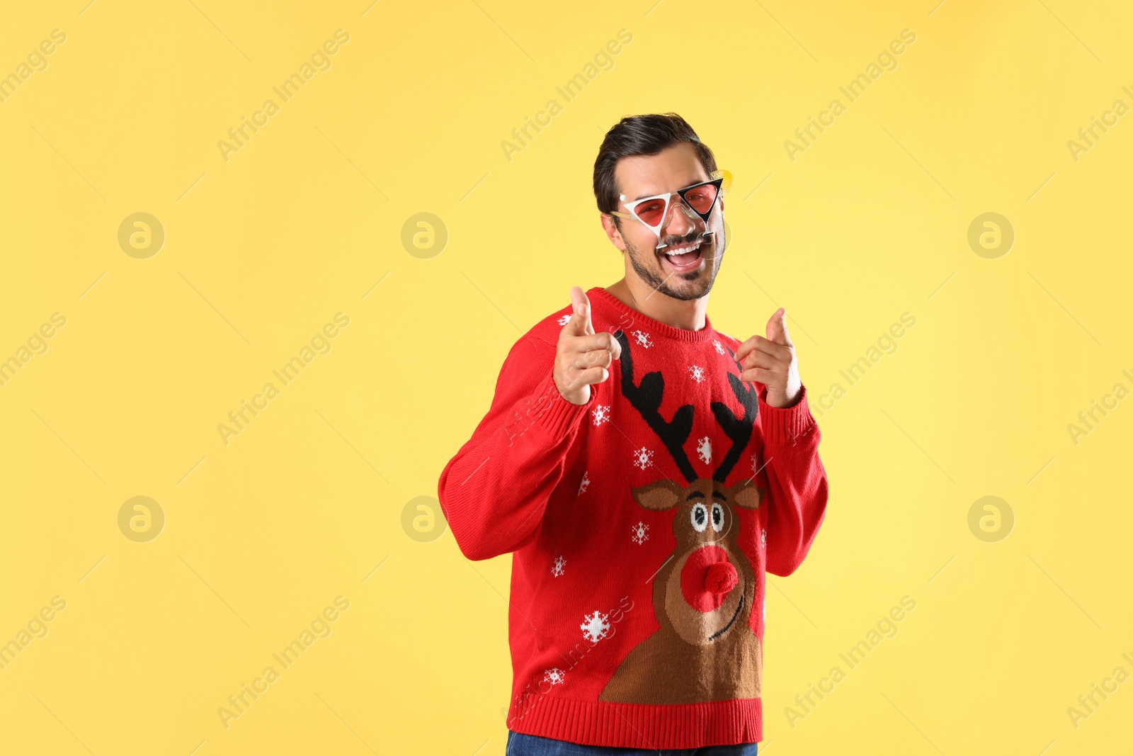 Photo of Happy man in Christmas sweater and party glasses on yellow background