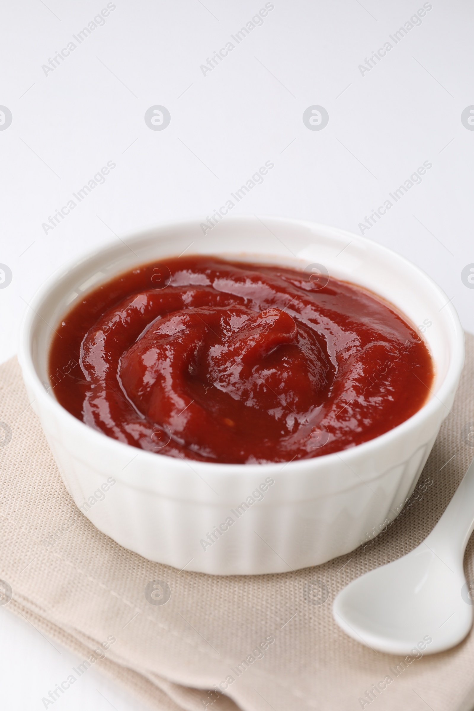 Photo of Organic ketchup in bowl and spoon on white table, closeup. Tomato sauce