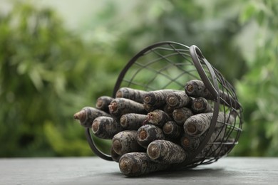 Photo of Raw black carrots in basket on grey table against blurred background