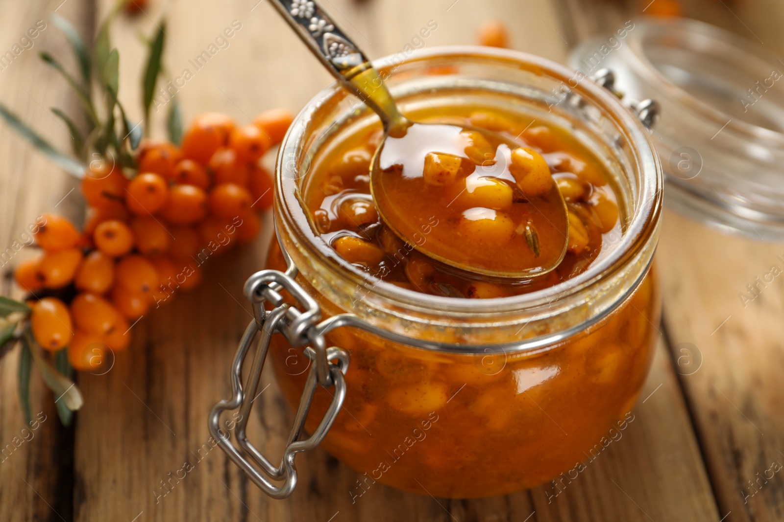 Photo of Delicious sea buckthorn jam and fresh berries on wooden table, closeup