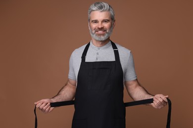 Happy man wearing kitchen apron on brown background. Mockup for design