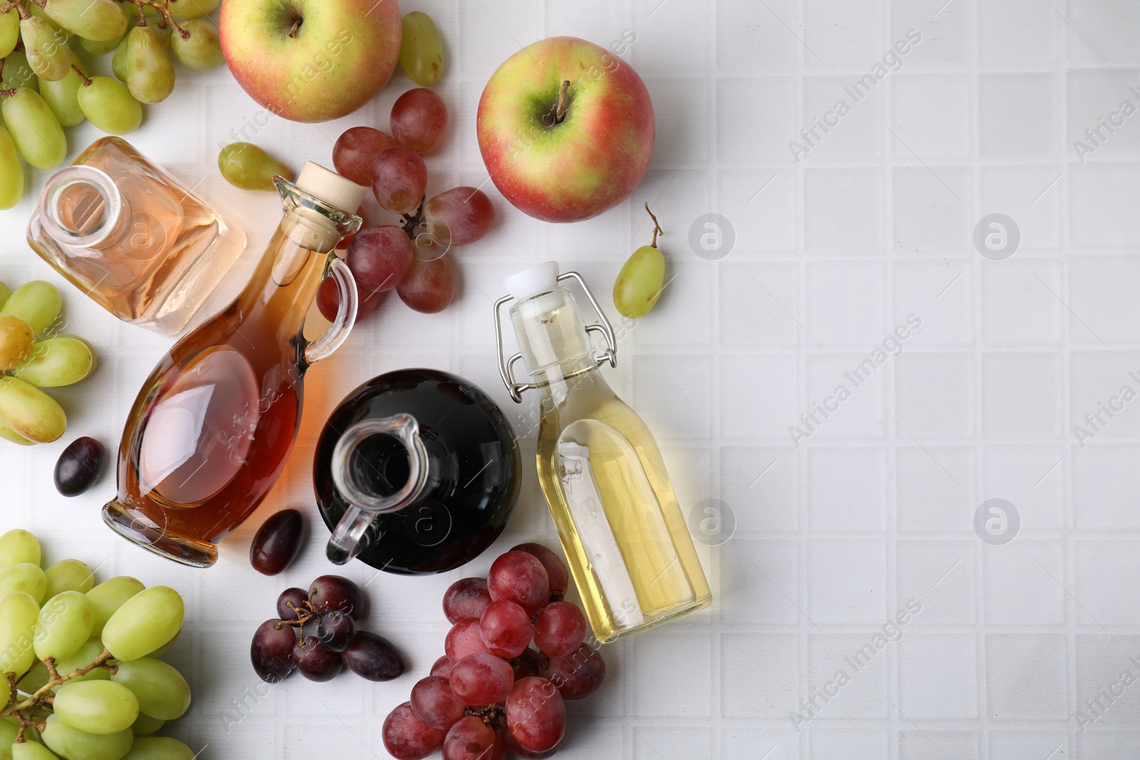 Photo of Different types of vinegar and ingredients on light tiled table, flat lay. Space for text