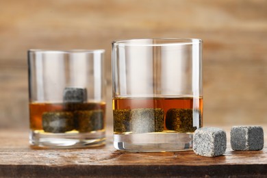 Photo of Whiskey stones and drink in glasses on wooden table, closeup