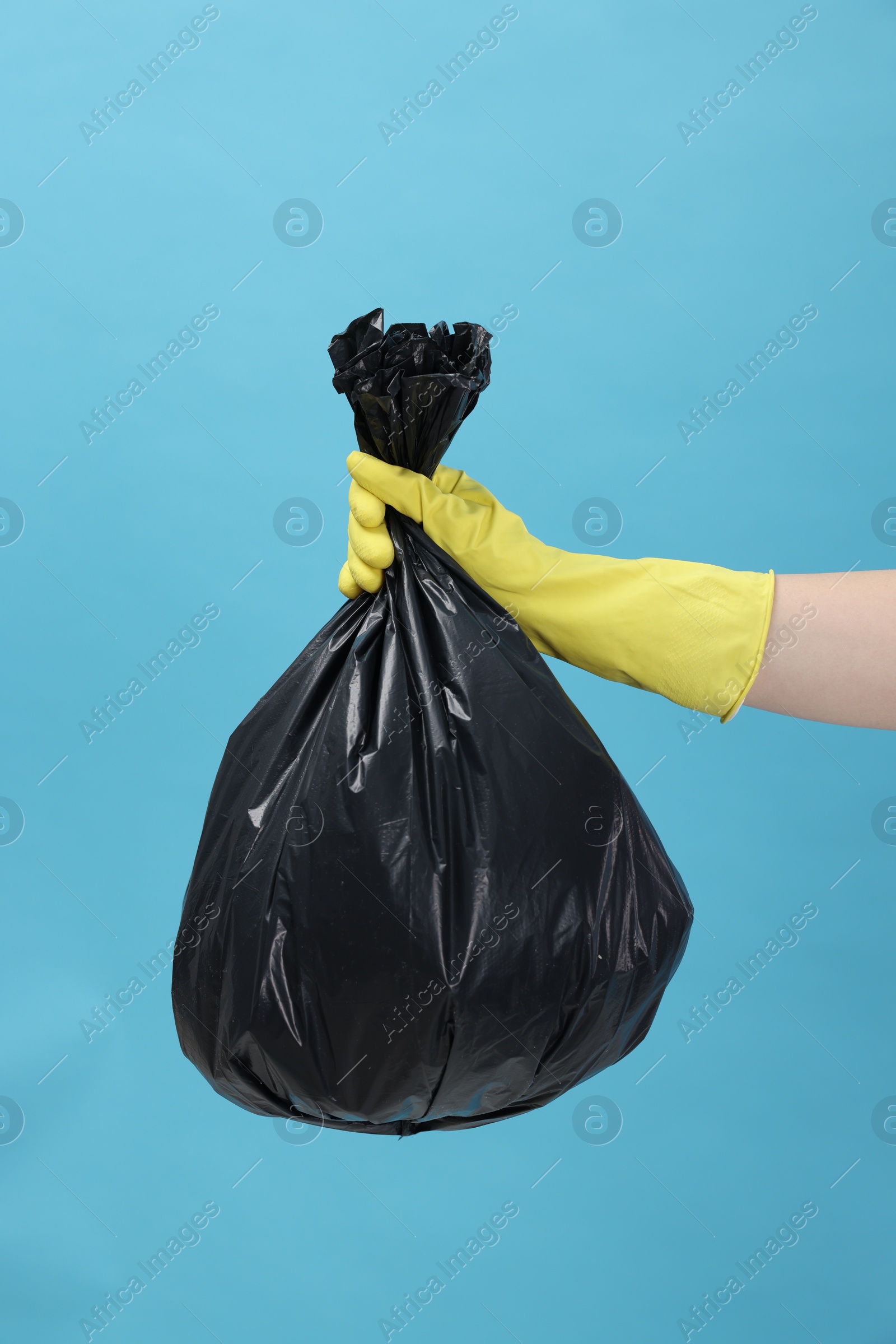 Photo of Woman holding plastic bag full of garbage on light blue background, closeup