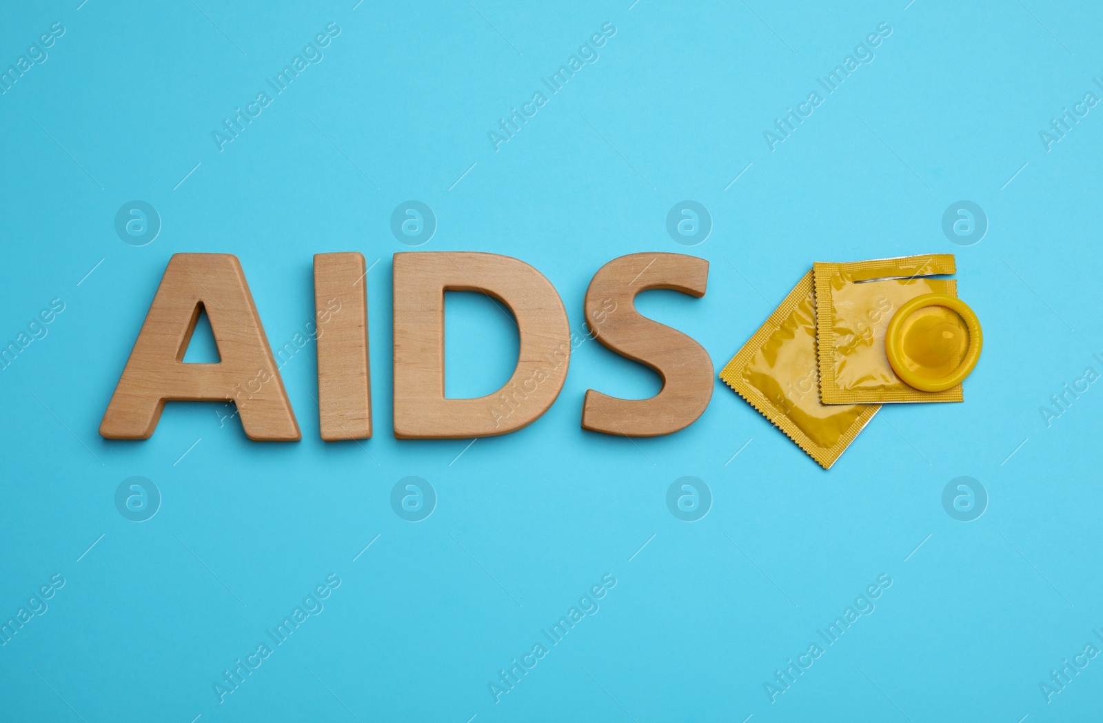 Photo of Yellow condoms and word AIDS made with wooden letters on light blue background, flat lay. Safe sex