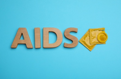 Yellow condoms and word AIDS made with wooden letters on light blue background, flat lay. Safe sex