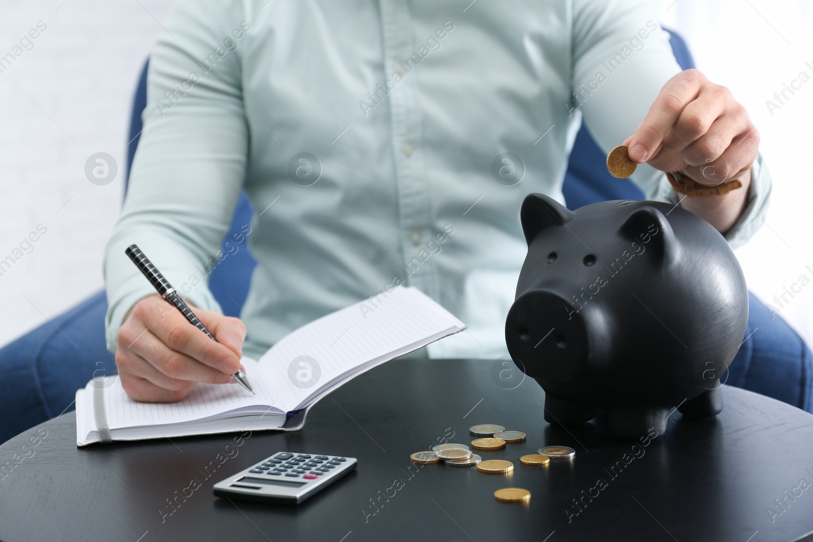 Photo of Businessman with notebook, piggy bank and money at table against light background, closeup