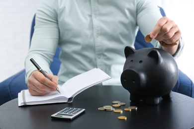 Photo of Businessman with notebook, piggy bank and money at table against light background, closeup