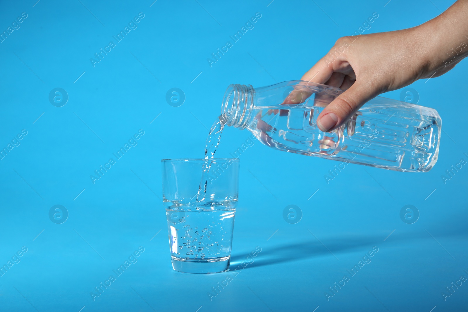 Photo of Woman pouring water from bottle into glass on blue background, closeup