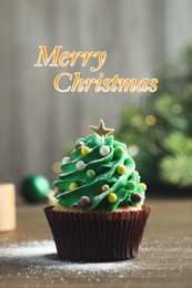 Image of Greeting card with phrase Merry Christmas. Festively decorated cupcake on wooden table