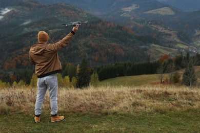 Photo of Young man with modern drone in mountains, back view. Space for text