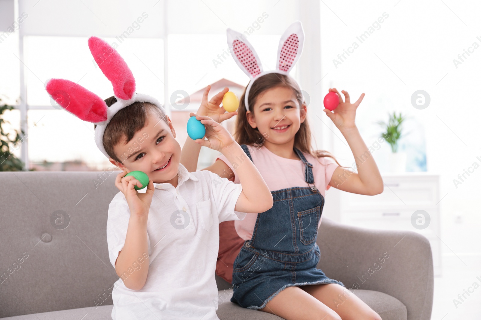 Photo of Cute little children in bunny ears headbands playing with Easter eggs at home
