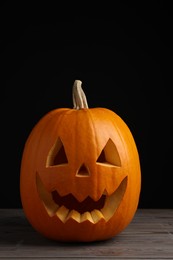 Photo of Scary jack o'lantern made of pumpkin on wooden table against black background. Halloween traditional decor