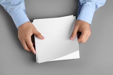 Photo of Man holding blank paper sheets for brochure at grey table, top view. Mock up