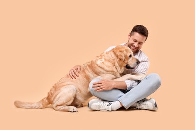 Photo of Man hugging with adorable Labrador Retriever dog on beige background. Lovely pet