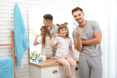 Photo of Little girl and her father brushing teeth together in bathroom at home. Space for text
