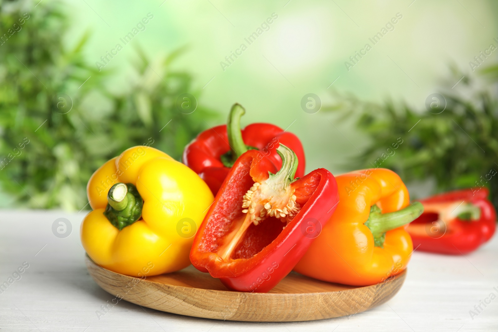 Photo of Wooden cutting board with ripe bell peppers on table against blurred background