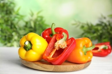 Photo of Wooden cutting board with ripe bell peppers on table against blurred background