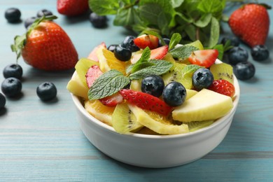 Photo of Tasty fruit salad in bowl and ingredients on light blue wooden table, closeup