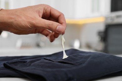 Photo of Man removing chewing gum from black jeans indoors, closeup. Space for text