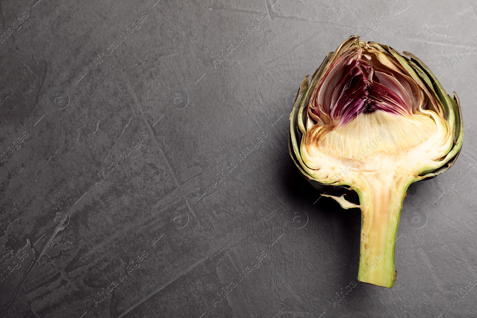 Photo of Cut fresh raw artichoke on grey table, top view