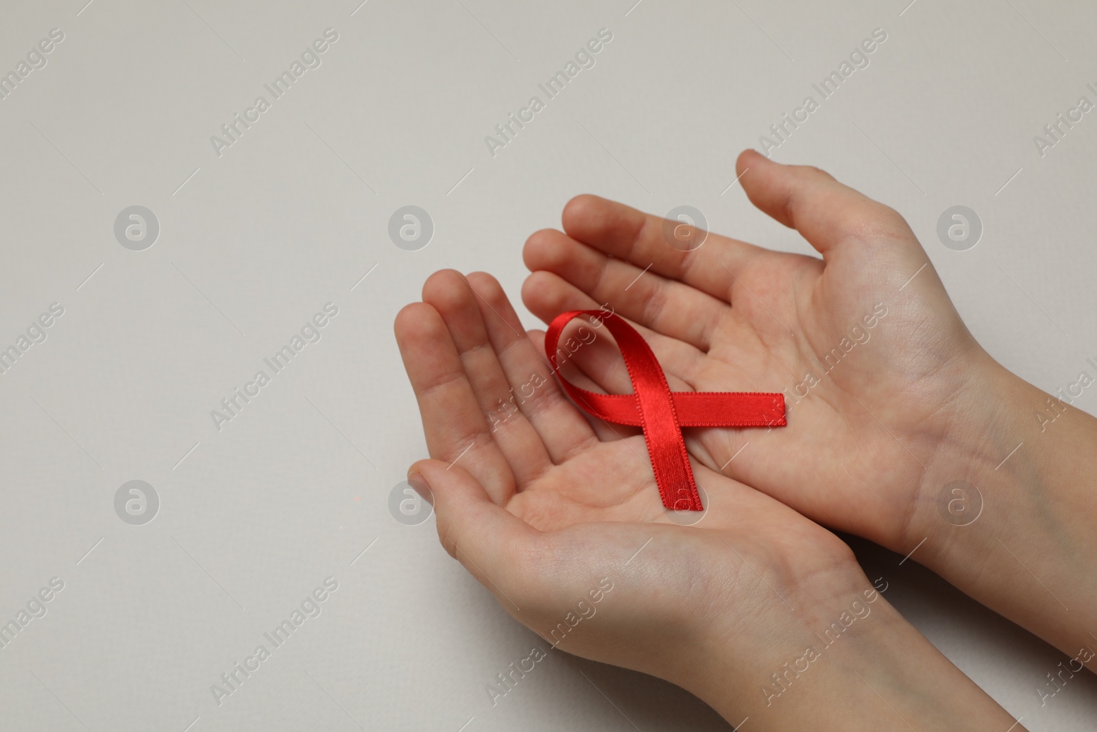 Photo of Little girl holding red ribbon on beige background, closeup with space for text. AIDS disease awareness