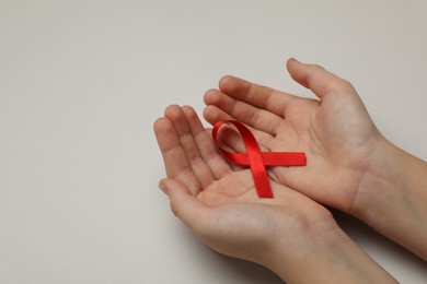 Little girl holding red ribbon on beige background, closeup with space for text. AIDS disease awareness