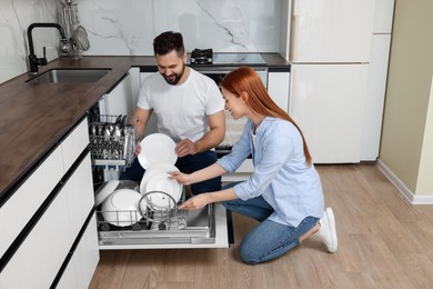 Photo of Happy couple loading dishwasher with plates in kitchen