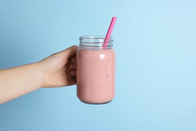 Photo of Woman holding mason jar with tasty smoothie and straw on light blue background, closeup