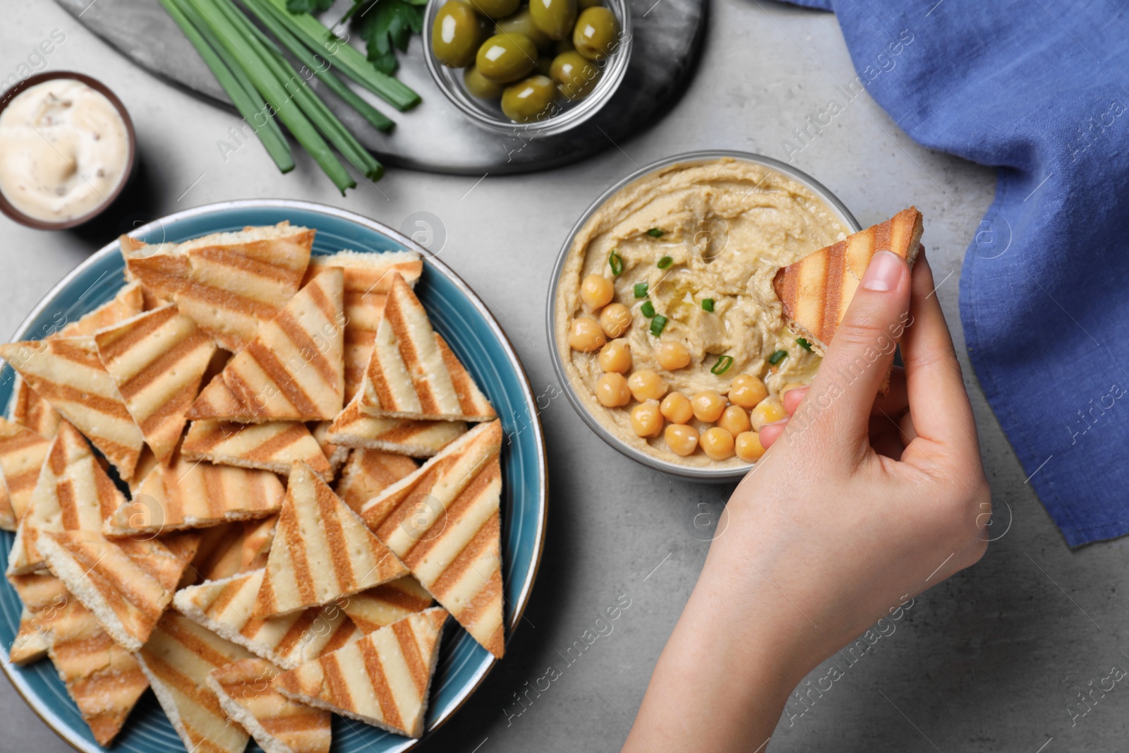 Photo of Woman dipping pita chip into hummus at grey table, top view