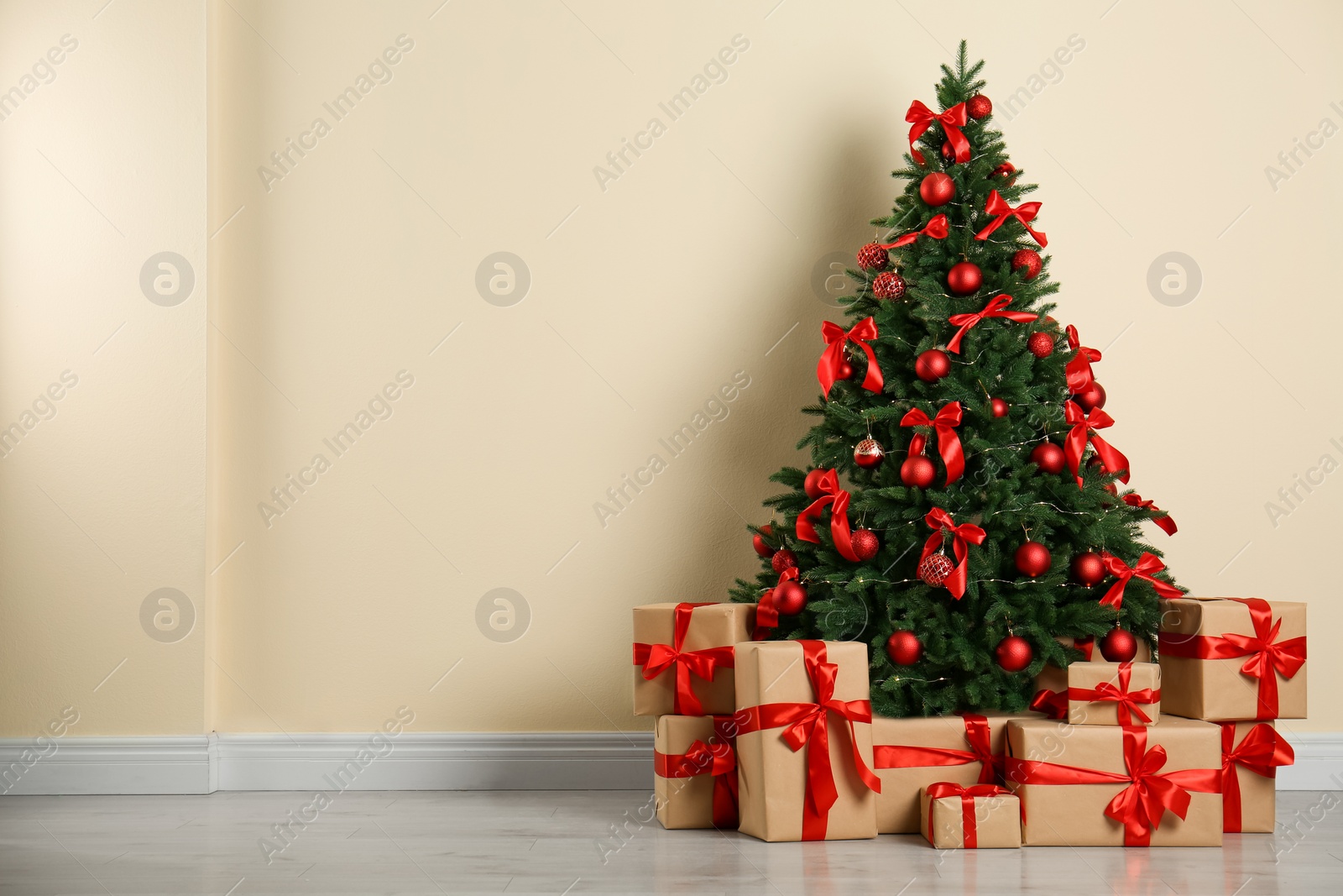 Photo of Decorated Christmas tree and gift boxes near beige wall. Space for text