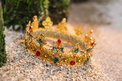 Photo of Beautiful golden crown on sand outdoors, closeup. Fantasy item