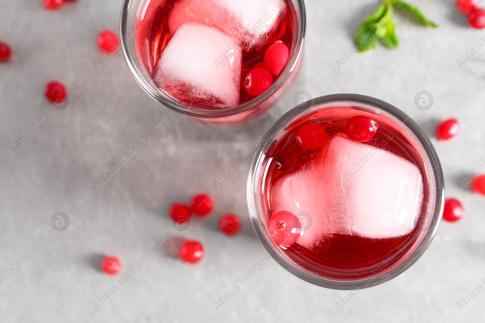 Photo of Tasty cranberry juice with ice cubes in glasses and fresh berries on light grey table, flat lay. Space for text